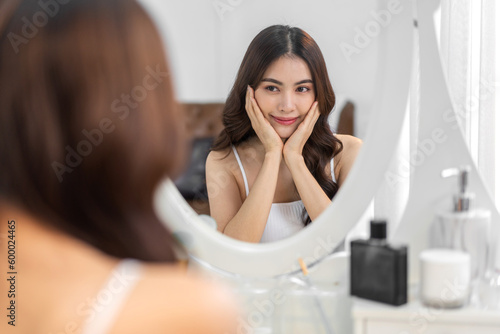 Smiling of beautiful asian woman fresh healthy white skin  clean  looking at mirror.asian girl touching on face applying cream  skincare  cosmetics  cosmetology  beauty  fashion at home.spa  wellness