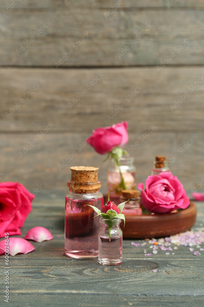 Bottles of cosmetic oil with rose extract and flowers on wooden table Bottles of cosmetic oil with rose extract and flowers on wooden table