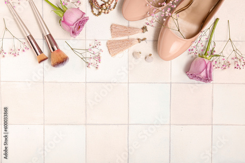 Composition with female accessories, heels, makeup brushes and flowers on light tile background