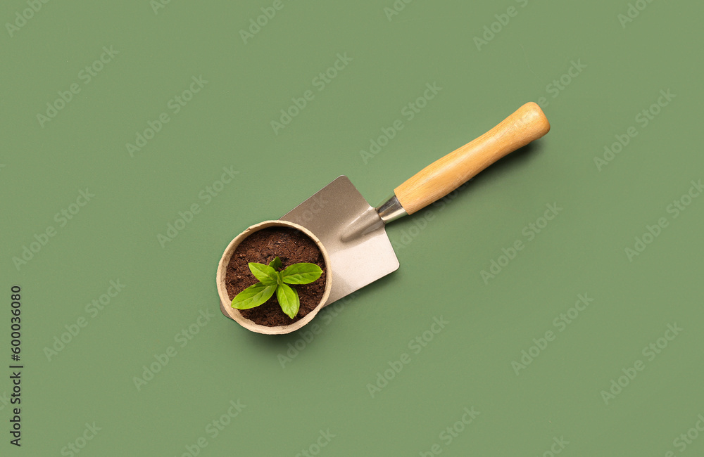 Peat pot with green seedling and shovel on green background - obrazy, fototapety, plakaty 