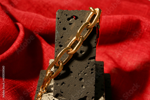 Decorative podium with beautiful chain bracelet on red fabric background