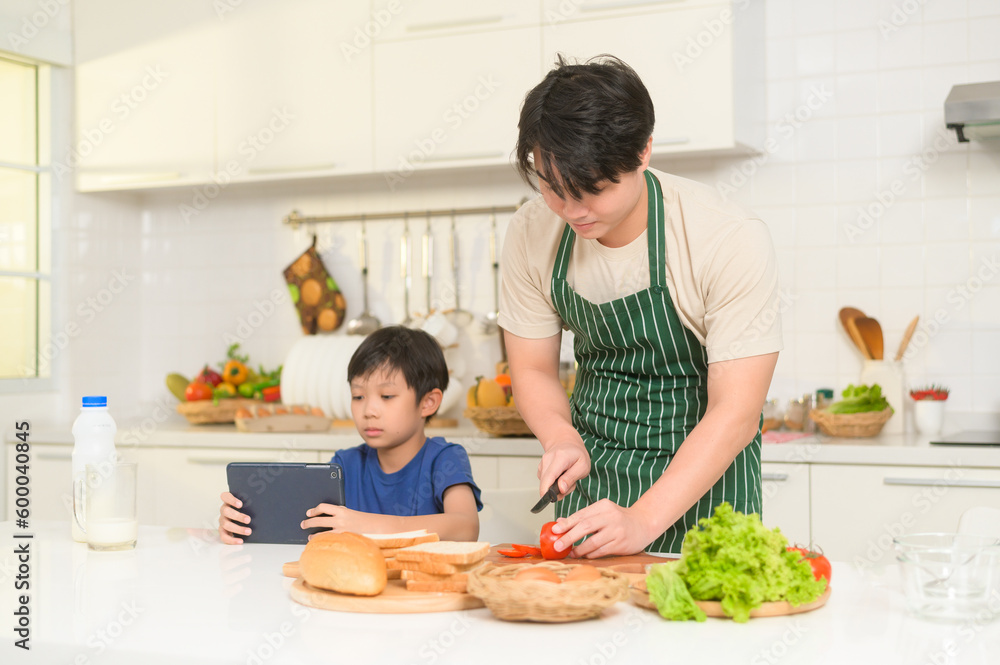 Happy Young Asian father making breakfast to his son in kitchen at home Happy Young Asian father making breakfast to his son in kitchen at home