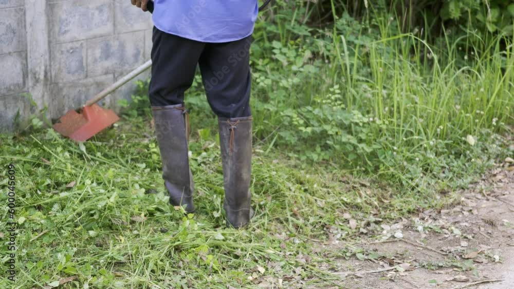 Working man wear boots mowing lawn with grass trimmer outdoors, Men