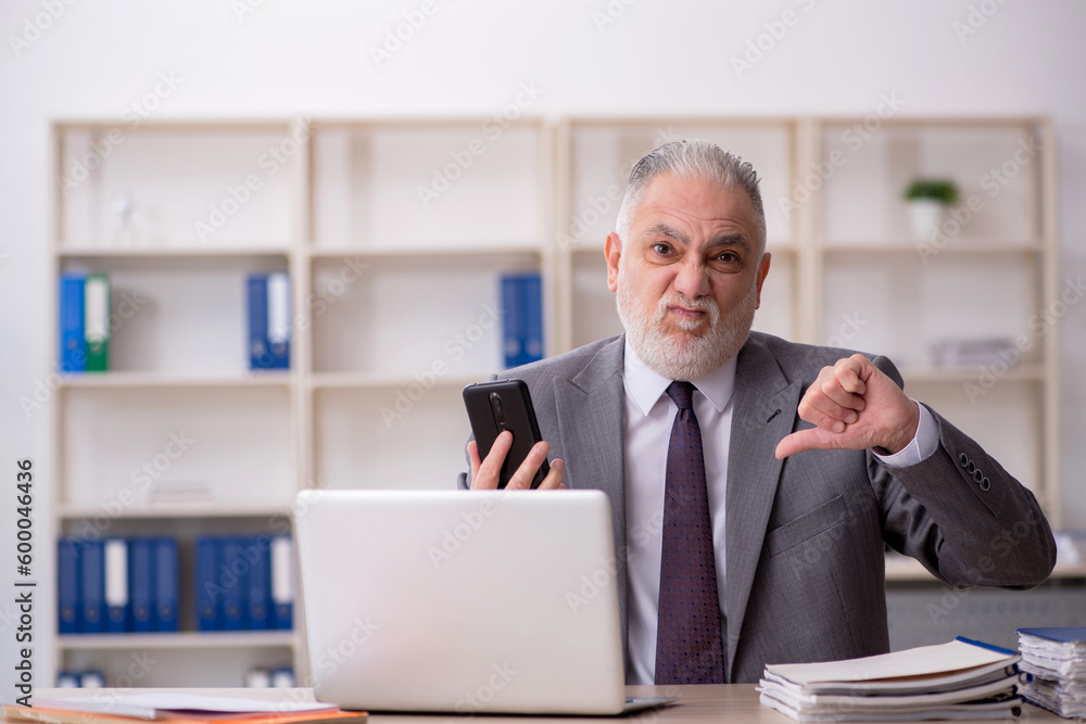 Old male employee speaking by phone at workplace Old male employee speaking by phone at workplace