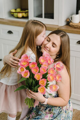 Daughter congratulates mother and gives bouquet of tulip flowers in kitchen at home. Mother's day concept. Mom hug child girl smiling and surprised. Greeting card. International Women's Day. Closeup