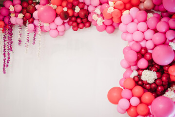 Arch with balloons, flowers for party. White photo wall decoration space or place with pink, red, maroon, burgundy balloons. Trendy spring decor. Celebration concept. Birthday party. Wedding reception