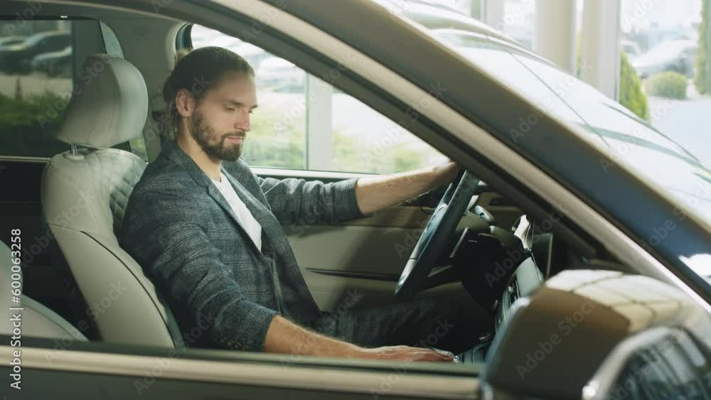 Happy caucasian man sitting inside new car and checking all function of new model at showroom. Male customer examining various auto at modern salon. Man examining car during visit at modern showroom. Happy caucasian man sitting inside new car and checking all function of new model at showroom. Male customer examining various auto at modern salon. Man examining car during visit at modern showroom.