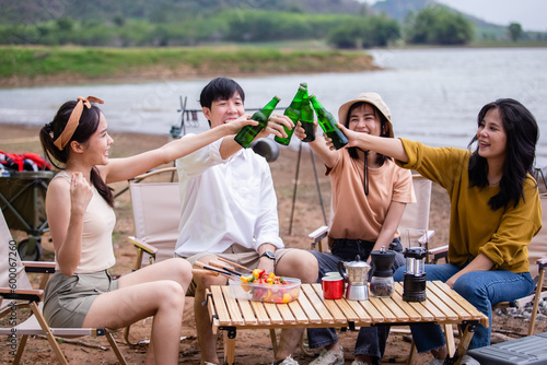 Group of young Asian friends party on vacation enjoy cheering with beer bottle. drinking at camping lake side. hands holding alcoholic beverages. Picnic in holiday. © eakgrungenerd