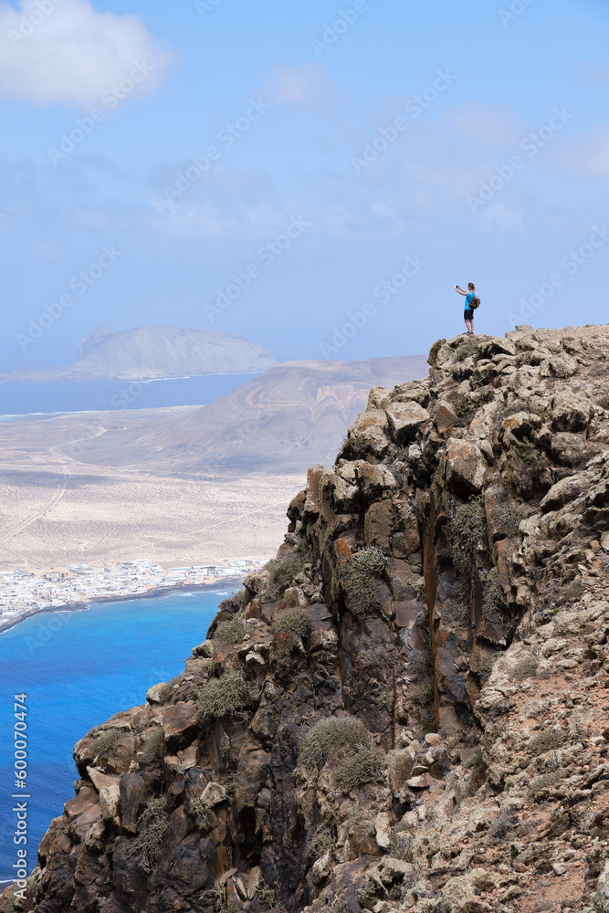 Woman photographing the landscape from a hill. La Graciosa Island in the background.