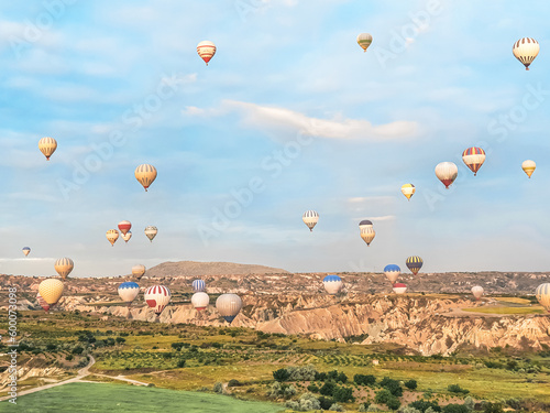 Flying in sky many bright colored beautiful balloons into air in Cappadocia in mountains early at sunrise, dawn. Filling balloon with hot air from burner, big basket. Tourists excursion, cloud flight