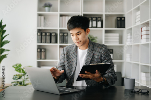 Asian business man executive manager looking at laptop watching online webinar training or having virtual meeting video conference doing market research working in modern office.