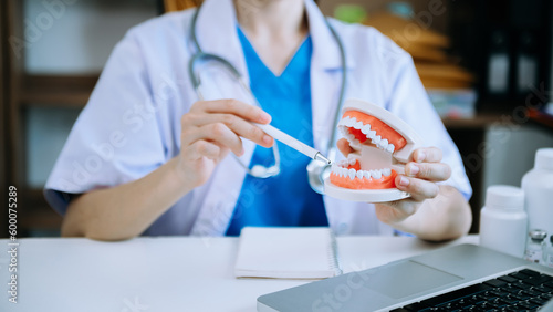 Concentrated dentist sitting at table with jaw samples tooth model and working with tablet and laptop in dental office professional dental clinic.