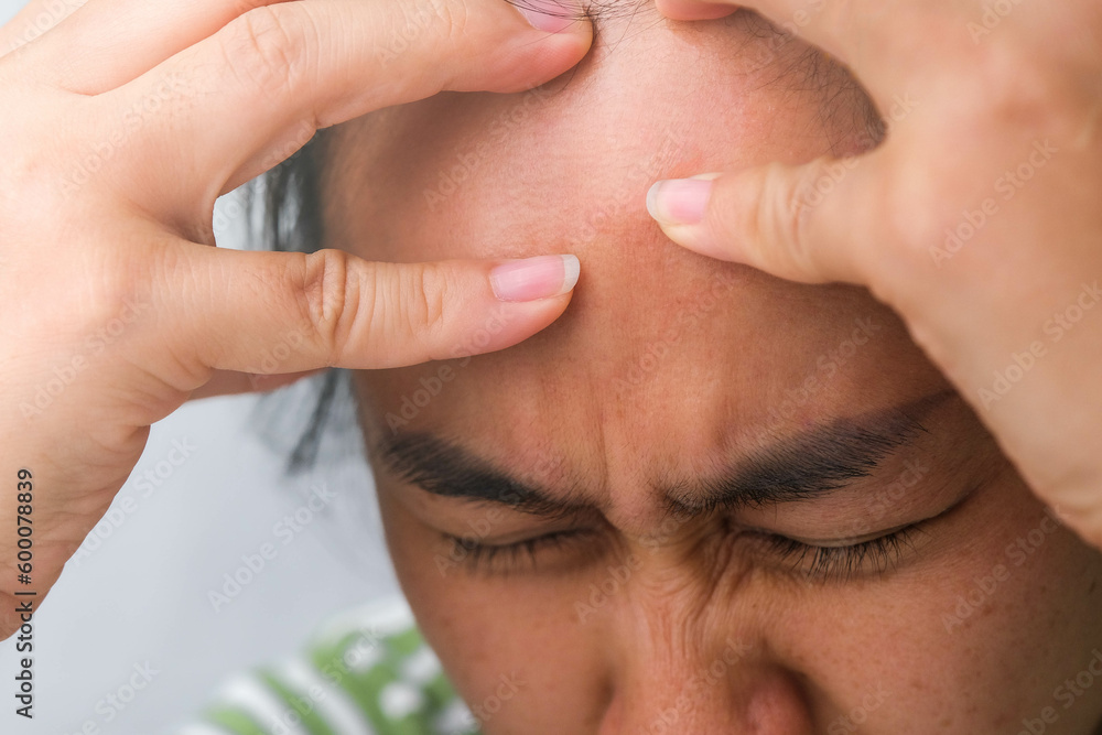 Young woman having headache against white curtain background in room. An adult woman touching head because of headache or migraine. Hands on head.
