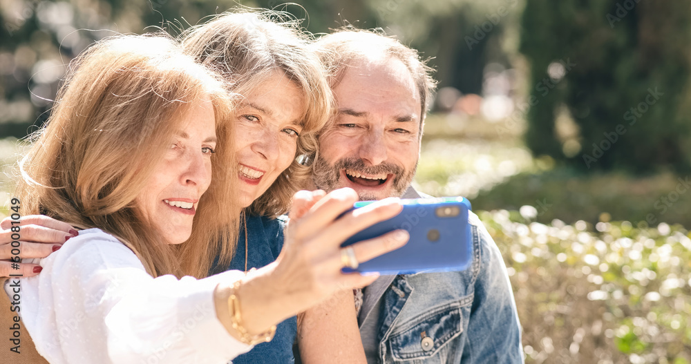 Happy mature friends recording video on cellphone in park Happy mature friends recording video on cellphone in park