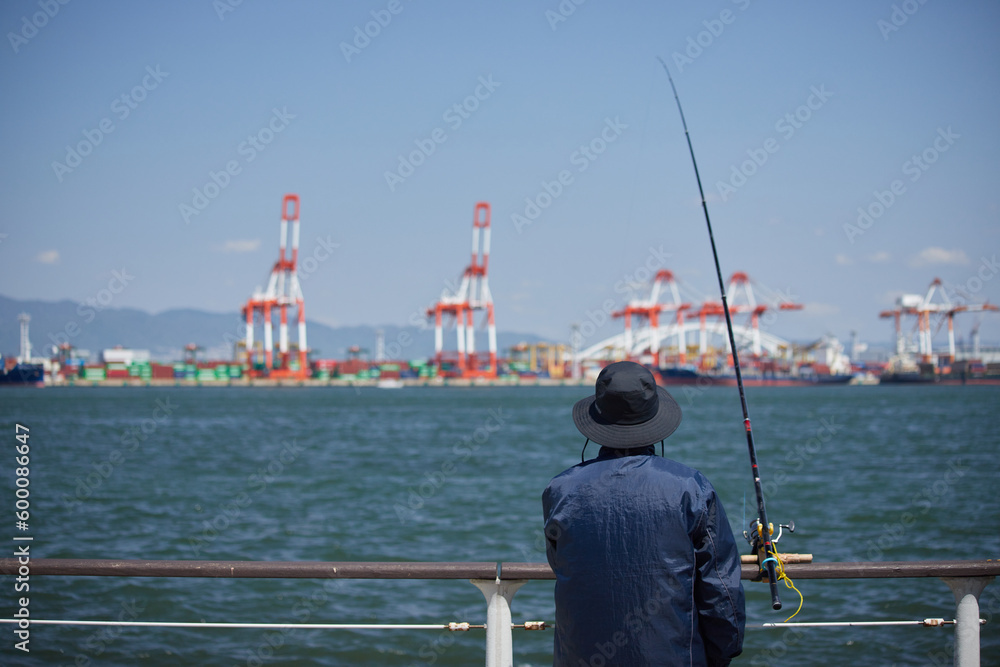昼の大阪湾の沿岸の公園で釣りをしている男性
