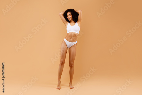 Full length shot of sensual young black lady posing in underwear with hands behind her head, showing perfect body shape