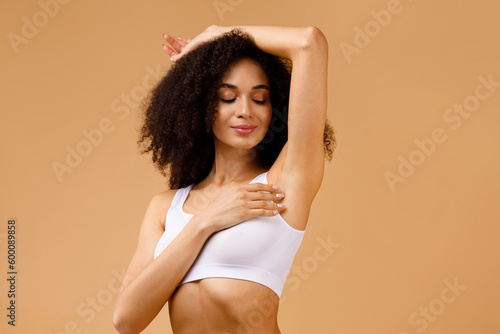 Young black woman with perfect soft armpit skin enjoying results of routine procedures, putting hand up photo
