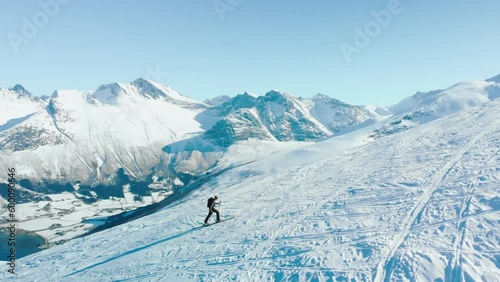 Inspiring and cinematic free ride skier concept. Solo backcountry rider slowly walk steep mountain side to approach face. Ski tour in Norwegian fjords. Mountaineering on epic snow mountain. photo