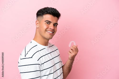 Young caucasian man holding invisaling isolated on pink background smiling a lot photo
