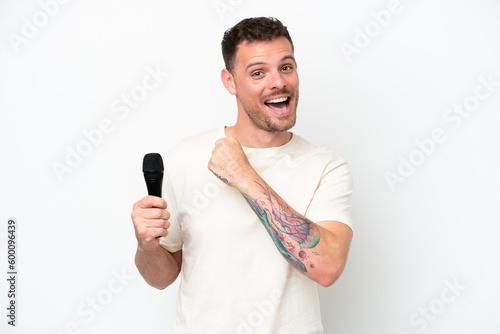 Young caucasian singer man picking up a microphone isolated on white background celebrating a victory