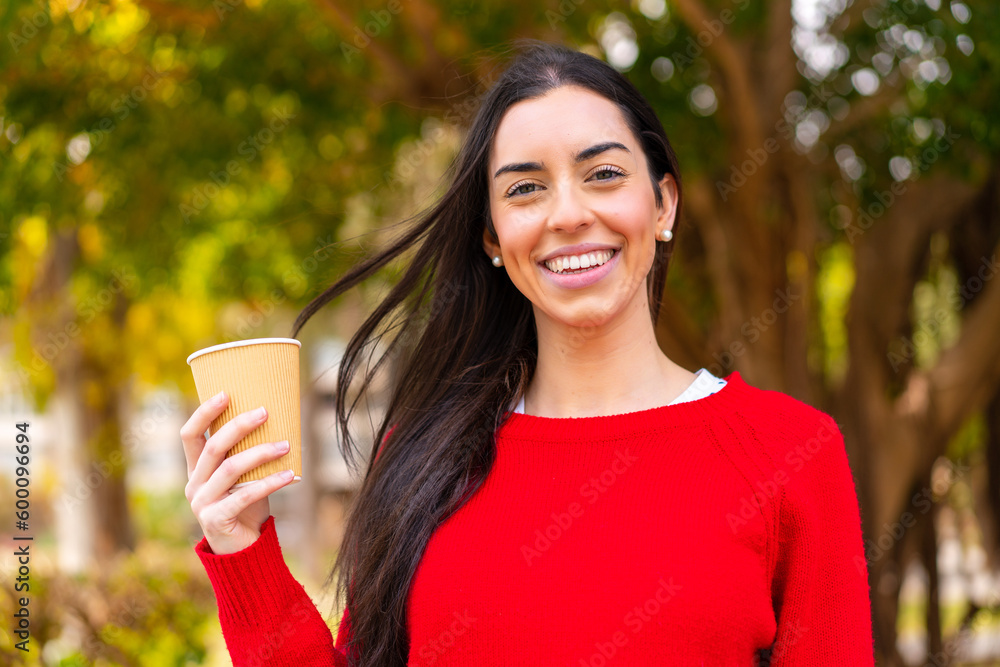 Young woman holding a take away coffee at outdoors smiling a lot