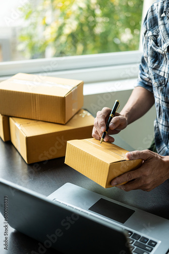 New Business Owner With Warehouse Package Delivery Box Prepares After Receiving Online Order From Social Media Customer On Laptop SME Business Idea © MrAshi