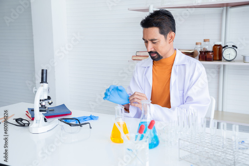 Asian male scientist wearing blue gloves for safe before mixing lab chemicals in science room, analysing Liquid Biochemicals in Laboratory Flask. Advanced Scientific Biotechnology Laboratory.