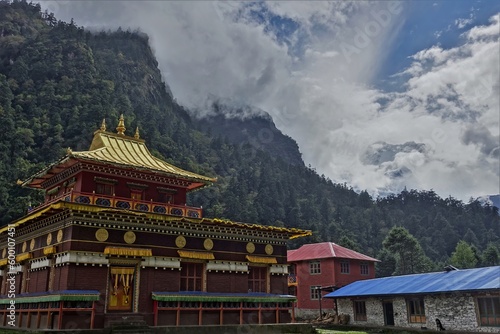 Tibetan-style main temple of Hinang Monastery, harmoniously blending with the ethereal presence of the hidden Manaslu Himalayas amidst the cloud cover.