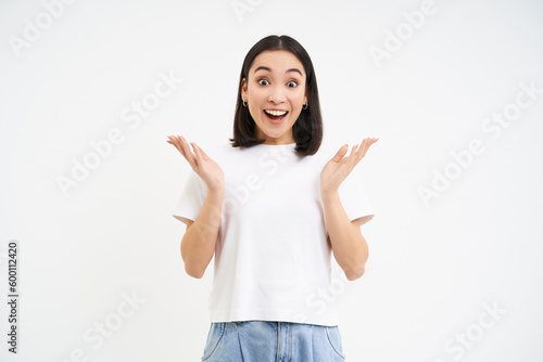 Enthusiastic asian woma, clap hands and smiles with surprised, happy face, congratulating, praising, standing over white background