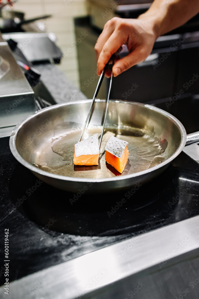 man chef cooking fried salmon fish in frying pan on kitchen man chef cooking fried salmon fish in frying pan on kitchen
