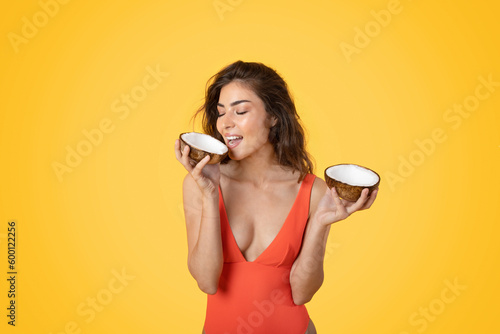 Smiling millennial asian woman in swimsuit biting coconut, enjoy free time #600122256