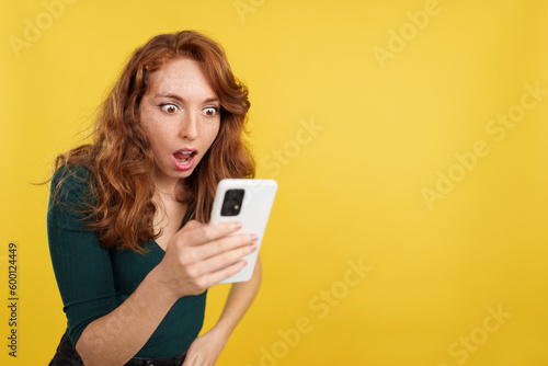 Surprised redheaded woman looking the screen of a mobile