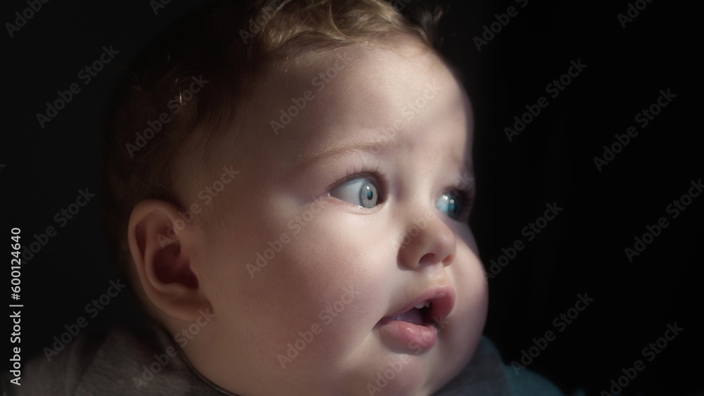 The baby is in the arms of his mother, looks with blue eyes. Millennial mother holds her son in her arms by the window of the house. The child's face in the sun. Close-up portrait The baby is in the arms of his mother, looks with blue eyes. Millennial mother holds her son in her arms by the window of the house. The child's face in the sun. Close-up portrait