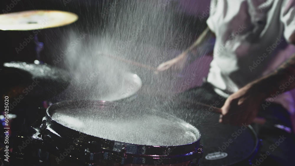The drummer hits the wet drum cymbal with his drumstick and the water