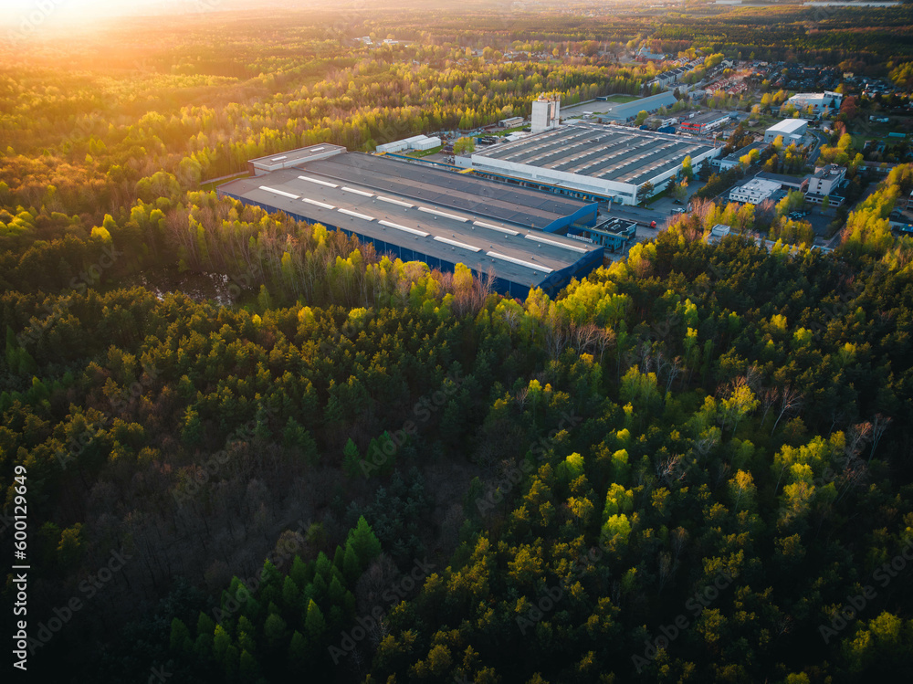 An industrial giant glows in the warmth of the setting sun. The aerial shot captures the magnitude of the building, surrounded by smaller structures. - obrazy, fototapety, plakaty 