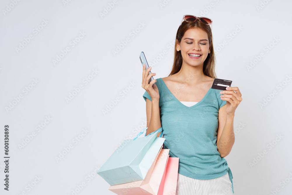 Happy young woman carrying shopping bags with using credit card and mobile phone standing over isolated on white background. Happy young woman carrying shopping bags with using credit card and mobile phone standing over isolated on white background.