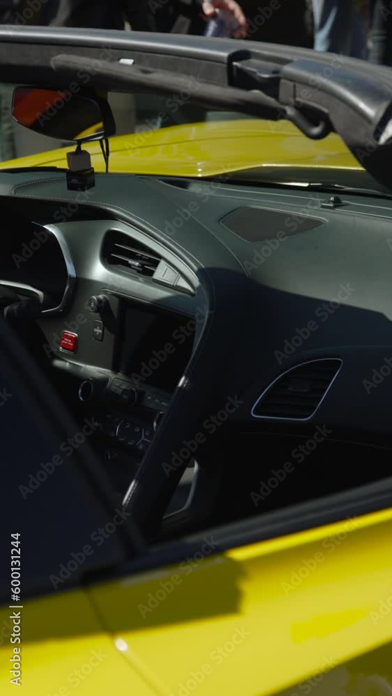 Dashboard and center console of American yellow convertible sports coupe with air ducts and engine start button. On sunny hot day, air freshener hangs on rearview mirror, vertical video. Dashboard and center console of American yellow convertible sports coupe with air ducts and engine start button. On sunny hot day, air freshener hangs on rearview mirror, vertical video.