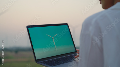 Feamle engineer holding laptop in hand. She looking 3d wind turbine design. photo