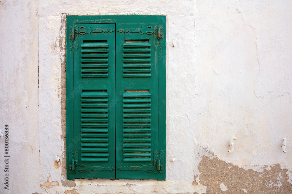 Old fashioned closed green wooden shutter on peeled white wall background. Cyclades Greece. Space