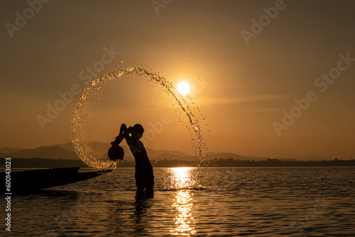 Silhouette of Fisherman catching fish in lake by using fishing net at beautiful