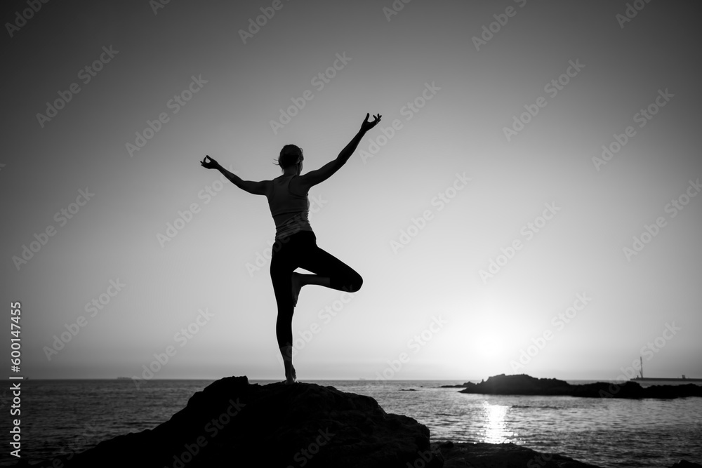 Silhouette of a yoga woman on the ocean shore. Black and white photo.