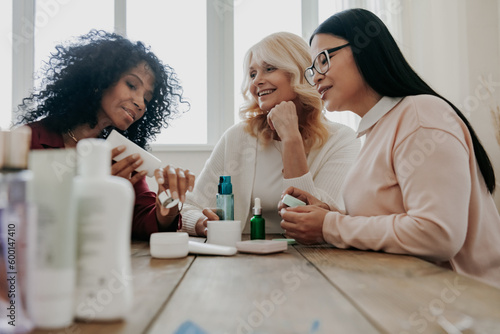 Three happy mature women testing beauty products while sitting at the desk together