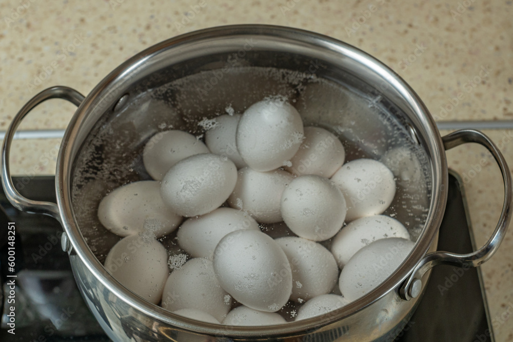 White chicken eggs are boiled in a stainless steel iron saucepan. White chicken eggs are boiled in bubbling hot water in a saucepan on a gas stove. Close-up top view White chicken eggs are boiled in a stainless steel iron saucepan. White chicken eggs are boiled in bubbling hot water in a saucepan on a gas stove. Close-up top view