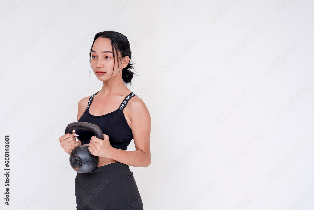 A determined and fit young woman weightlifting by holding a kettle bell, side view. Isolated on a white background. A determined and fit young woman weightlifting by holding a kettle bell, side view. Isolated on a white background.