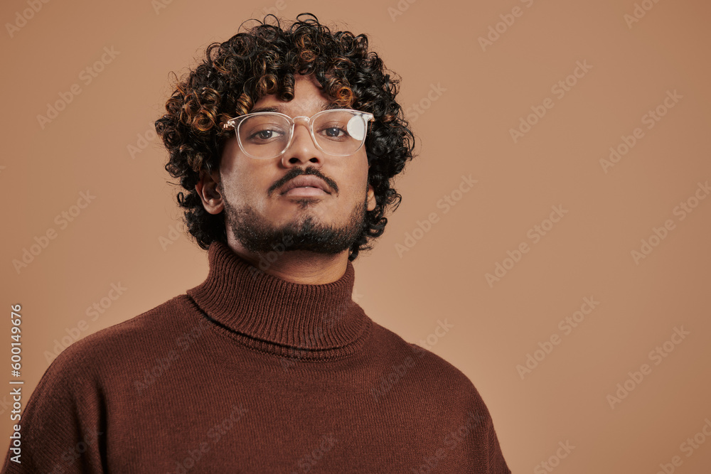 Portrait of handsome Indian man in eyeglasses looking at camera against brown background Portrait of handsome Indian man in eyeglasses looking at camera against brown background
