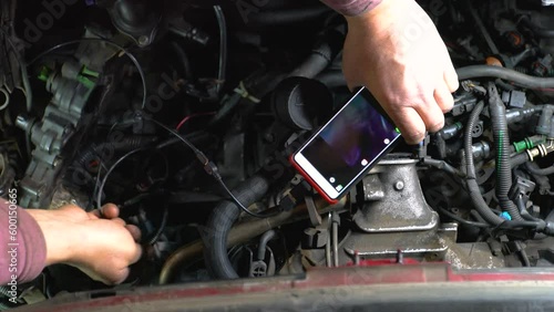 Hands of car mechanic check the vehicle engine with technical endoscope with rotary camera and mobile phone. Repair of engine head and valves. photo