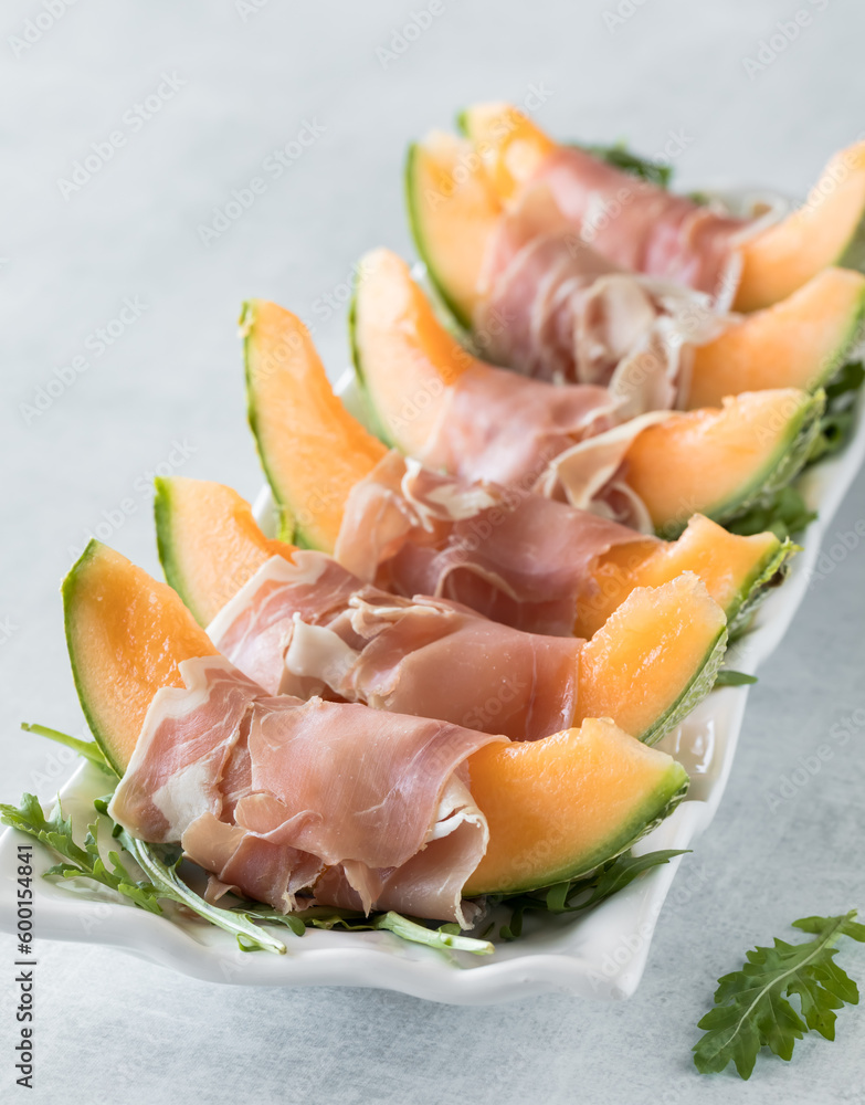 Cantaloupe wedges wrapped in prosciutto on a platter of arugula.