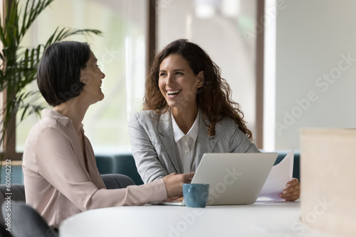 Принти на полотні Two happy businesswomen, office employees work in office, laughing, joking during workflow, share creative ideas, solution feel satisfied with corporation, engaged in teamwork