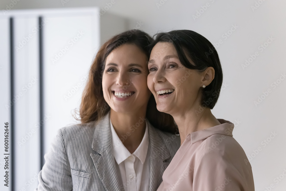 Beautiful mature Caucasian and young Hispanic businesswomen colleagues in elegant formal wear staring aside smiling posing indoors, feel happy, photoshoot for corporate album. Friendship at workplace Beautiful mature Caucasian and young Hispanic businesswomen colleagues in elegant formal wear staring aside smiling posing indoors, feel happy, photoshoot for corporate album. Friendship at workplace