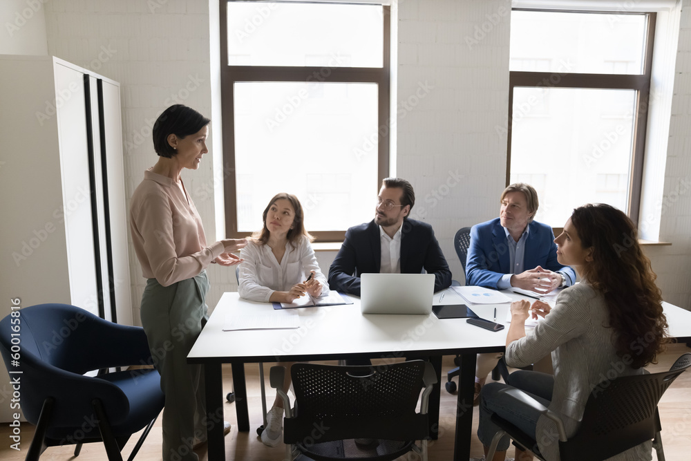 Mature businesswoman makes speech stand in front of company clients, business trainer leads corporate training for staff members, take part negotiations or group meeting or briefing in conference room